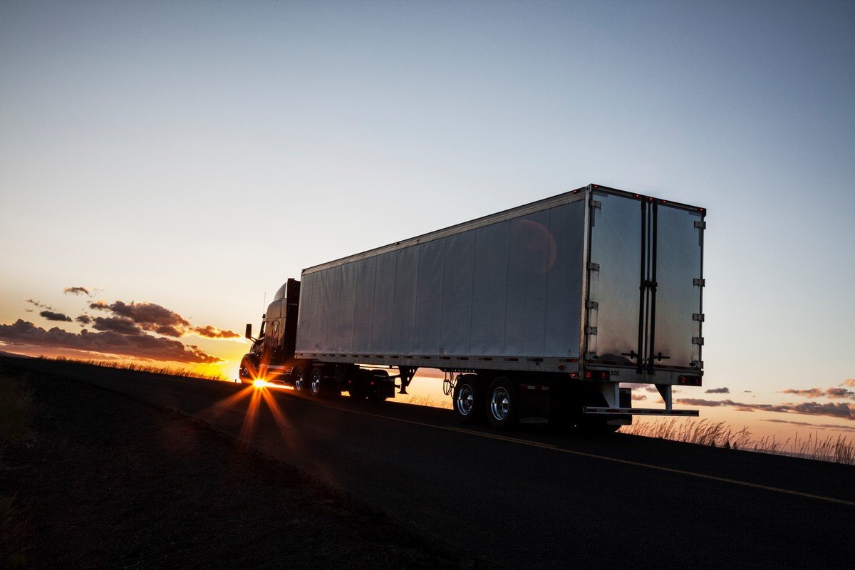 Silhouette of a commercial truck driving on a highway at sunset